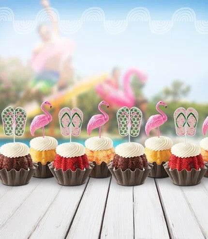 Bundtinis with flamingo and sunglasses toppers on a table poolside.