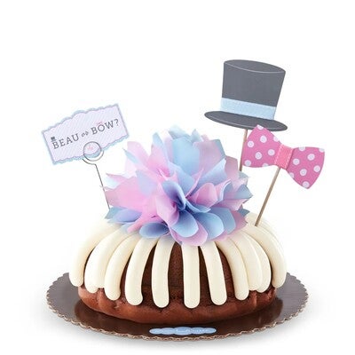 Bundt Cake with cream cheese frosting, with Baby Gender Reveal decoration with top hat pink and white polka dotted bow-tie, pink, white and blue paper bow and a decorative card with beau or bow written on it.