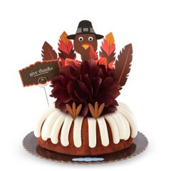 A large Carrot bundt cake with a chocolate colored bow in the center and a whimsical turkey cutout with 5 Gratitude Feathers. 