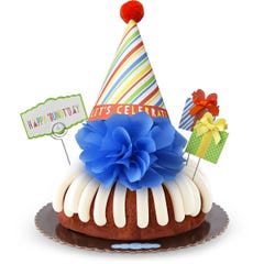 A bundt cake with frosting topped with a party hat that says Let's Celebrate. Two wrapped gift boxes are on the sides along with a card that reads Happy 'Bundt'day.
