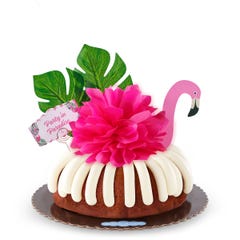 A Carrot bundt cake decorated with a pink flamingo with tropical leaves. It also includes a card that reads Party in Paradise. 