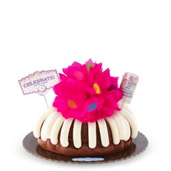 Large decorated bundt cake covered with frosting. Decoration includes a pink bow with confetti sprinkles and a confetti popper with a card that says Celebrate and cue the confetti. 