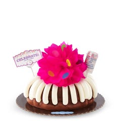 Large decorated bundt cake covered with frosting. Decoration includes a pink bow with confetti sprinkles and a confetti popper with a card that says Celebrate and cue the confetti. 