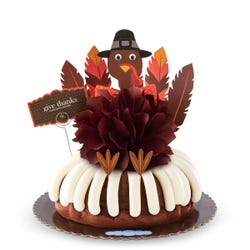 A large bundt cake with a chocolate colored bow in the center and a whimsical turkey cutout with 5 Gratitude Feathers. 