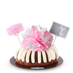 A bundt cake topped with a pink bow and adorned with soft white wings. 