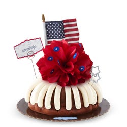 A large bundt cake with a red satin bow in the center with stickers of stars. There are also two star shaped sparkler candles and an American flag with a card that says stars and stripes.