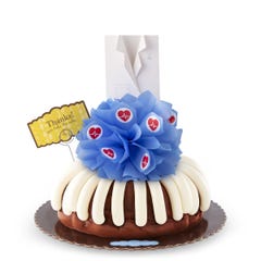 A decorated bundt cake with frosting. The center includes a blue bow with heartbeat stickers and a white lab coat and a card that reads Thanks! You take the cake.