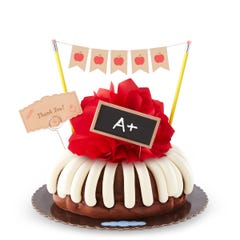 A frosted bundt cake with a red bow in the center. The cake is decorated with a chalkboard with an A+ written on it along with a card that reads Thank You!.