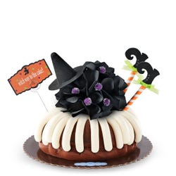 Last Chance! This bundt cake is decorated with frosting all around. It is topped with a black bow with a witch hat and legs sticking out of the cake. A card is attached and reads witch way to the cake?.