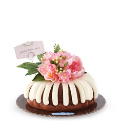 Bundt cake decorated with a beautiful pink flower arrangement with greenery. A card reads yours, mine, ours.