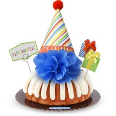 A bundt cake with frosting topped with a party hat that says Let's Celebrate. Two wrapped gift boxes are on the sides along with a card that reads Happy 'Bundt'day.