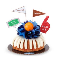 A confetti bundt cake with frosting, decorated with a mini basketball on top of a bow with different shades of blue in the center of the cake. The cake also contains a We're #1 foam finger, a flag that says All Star and a card that says MVP.
