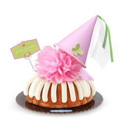 A confetti bundt cake with frosting, topped with a pink bow and a princess-themed pink party hat with a butterfly on top. A card on the cake reads Prettiest Princess.