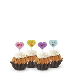 Mini Bundt cakes with white frosting, topped with conversation hearts in pink, lime, lavender, and light teal, displaying messages: XOXO, LOVE YOU, SWEET, and CUTIE PIE.