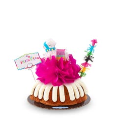 A party-themed bundt cake with a colorful mini piñata at the center and a piñata stick next to it. The cake has a card that reads FIESTA. 