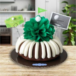 A golf themed bundt cake with a green bow in the center to represent the green grass with a small golf ball. A card reads hole in one. 