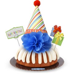 A bundt cake with frosting topped with a party hat that says Let's Celebrate. Two wrapped gift boxes are on the sides along with a card that reads Happy 'Bundt'day.