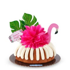 A Lemon bundt cake decorated with a pink flamingo with tropical leaves. It also includes a card that reads Party in Paradise. 
