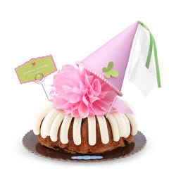 An Oreo Cookies & Cream bundt cake with frosting, topped with a pink bow and a princess-themed pink party hat with a butterfly on top. A card on the cake reads prettiest princess.