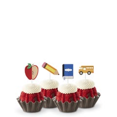Red Velvet flavored mini Bundt cakes (Bundtinis®) topped with creamy white frosting, accompanied by school-themed toppers: a sliced apple, a pencil, a notebook, and a yellow school bus.