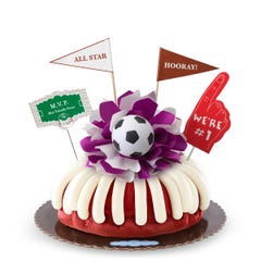 A Red Velvet bundt cake, decorated with a mini soccer ball on top of a purple and white bow in the center of the cake.