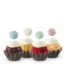 Cupcake-sized Bundt cakes topped with creamy white frosting. Each has a fluffy pom-pom topper in shades of sky blue, white, mint green, and soft rose.