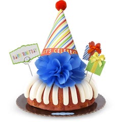 A bundt cake with frosting topped with a party hat that says Let's Celebrate. Two wrapped gift boxes are on the sides along with a card that reads Happy 'Bundt'day.