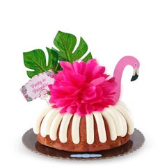 A Strawberries & Cream bundt cake decorated with a pink flamingo with tropical leaves. It also includes a card that reads Party in Paradise. 