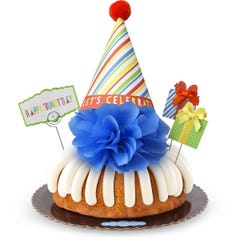A bundt cake with frosting topped with a party hat that says Let's Celebrate. Two wrapped gift boxes are on the sides along with a card that reads Happy 'Bundt'day.