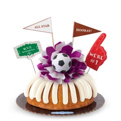 A Vanilla bundt cake with frosting, decorated with a mini soccer ball on top of a purple and white bow in the center of the cake. The cake also contains a We're #1 foam finger, a flag that says All Star and a card that says M.V.P.