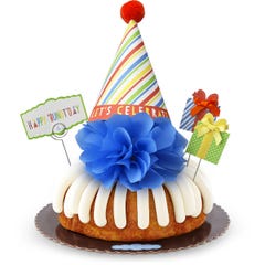 A bundt cake with frosting topped with a party hat that says Let's Celebrate. Two wrapped gift boxes are on the sides along with a card that reads Happy 'Bundt'day.