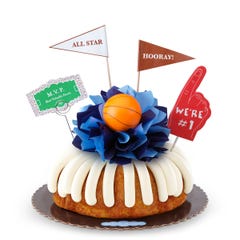 A bundt cake with frosting, decorated with a mini basketball on top of a bow with different shades of blue in the center of the cake.