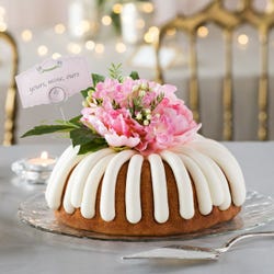 Bundt cake decorated with a beautiful pink flower arrangement with greenery. A card reads yours, mine, ours.